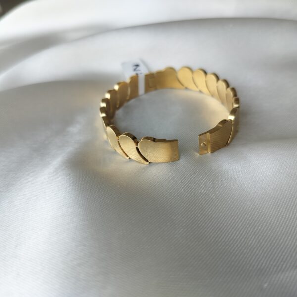 Close-up of luxury oval gold-tone comma-link bracelet, showcasing its smooth hinge mechanism and intricate linked design