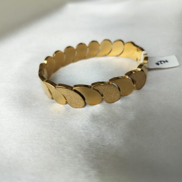 Close-up of oval gold bracelet showing alternating textured and smooth comma-links with visible hinge clasp